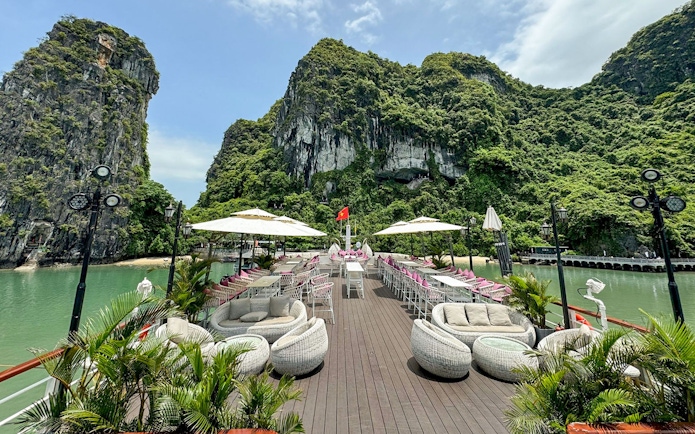 Cruise deck with seating and umbrellas, surrounded by Ha Long Bay limestone cliffs.