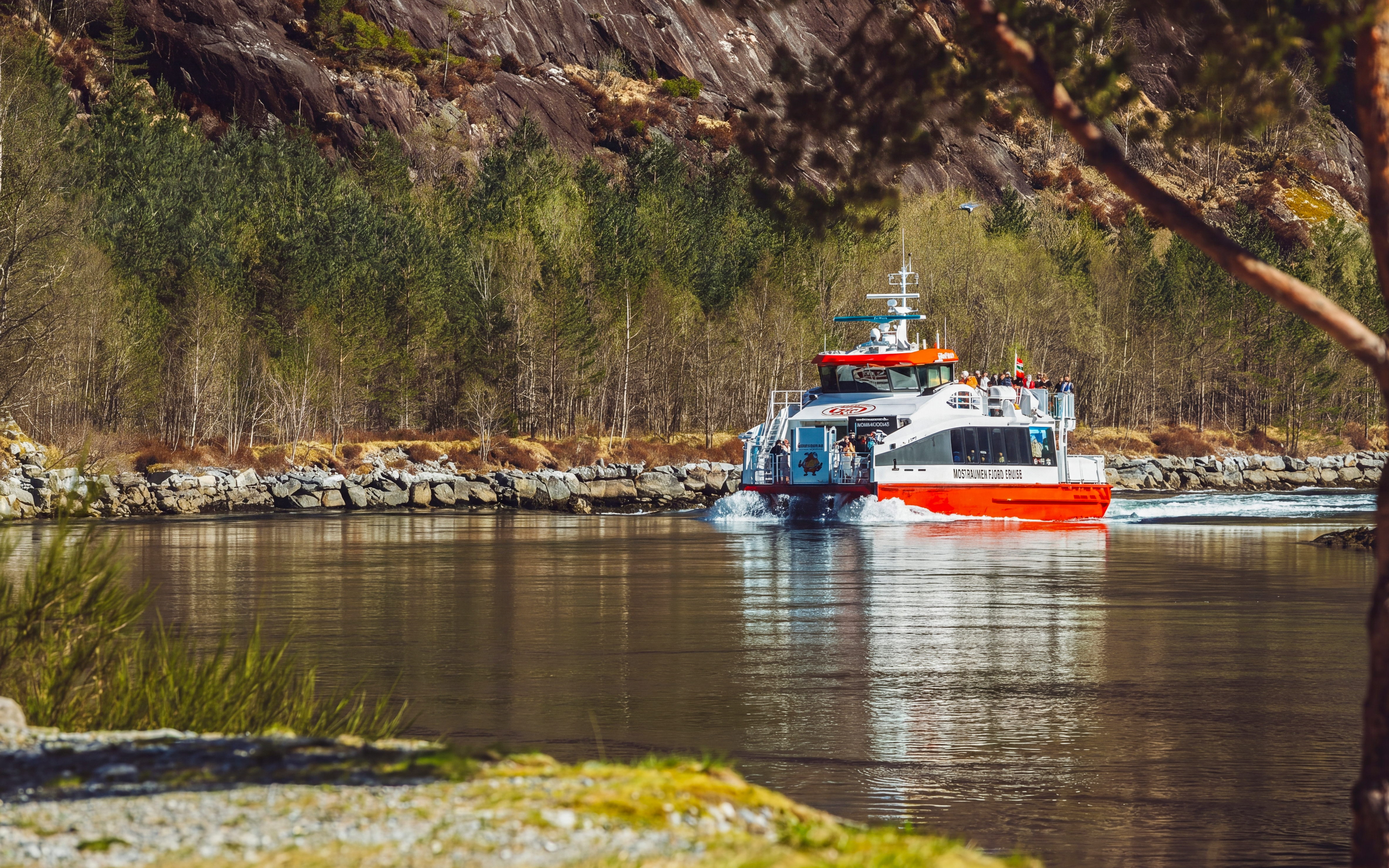Cruise boat on Mostraumen Fjord near Bergen, surrounded by rocky cliffs and forest.