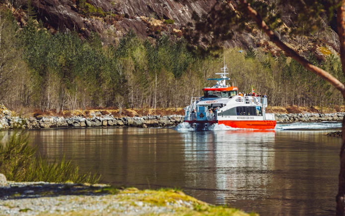 Cruise boat on Mostraumen Fjord near Bergen, surrounded by rocky cliffs and forest.