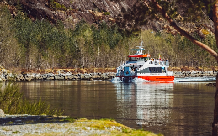 Cruise boat on Mostraumen Fjord near Bergen, surrounded by rocky cliffs and forest.