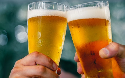 Two hands clinking beer glasses at A'DAM LOOKOUT with city view.