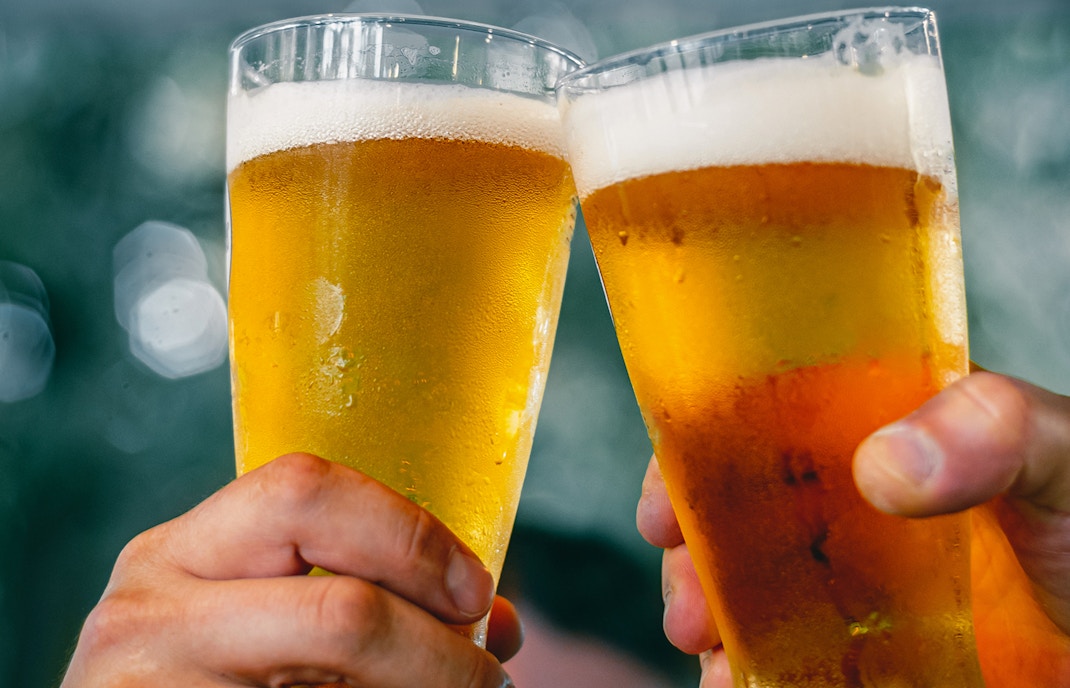 Two hands clinking beer glasses at A'DAM LOOKOUT with city view.