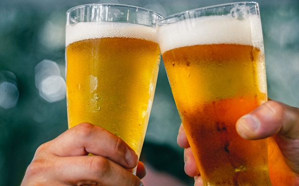 Two hands clinking beer glasses at A'DAM LOOKOUT with city view.