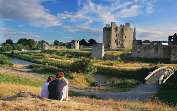 Couple sitting on a hill overlooking Trim Castle in County Meath, Ireland.