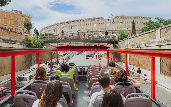 Open-top sightseeing bus approaching the Colosseum in Rome.