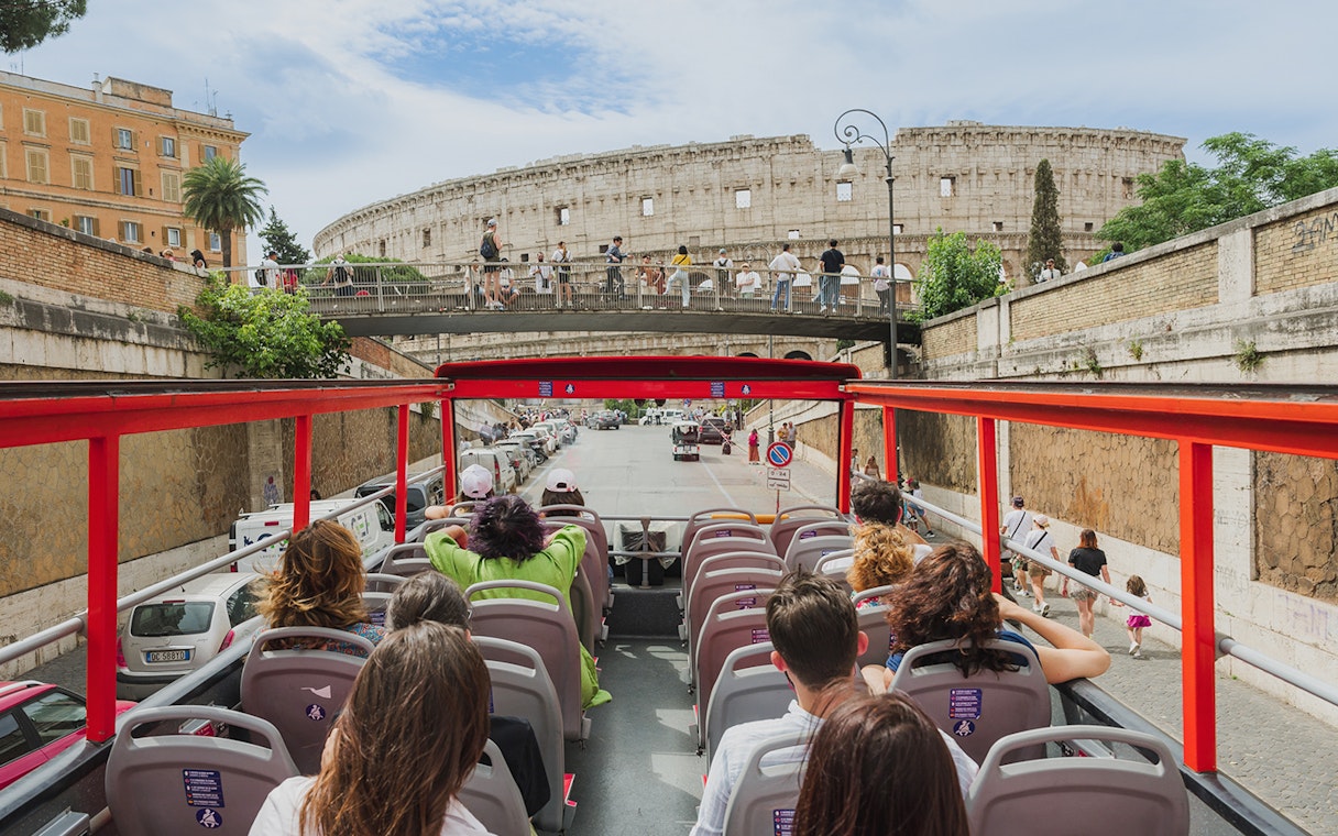 Open-top sightseeing bus approaching the Colosseum in Rome.