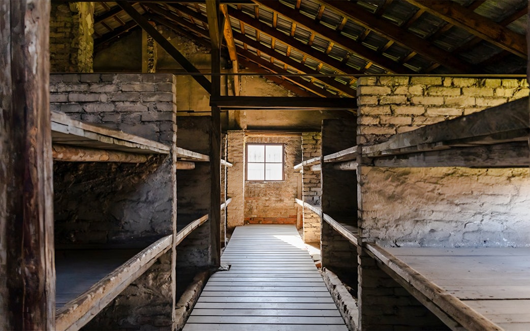 Auschwitz-Birkenau I barracks interior with wooden bunks and brick walls.