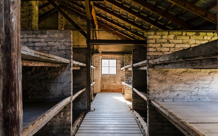 Auschwitz-Birkenau I barracks interior with wooden bunks and brick walls.