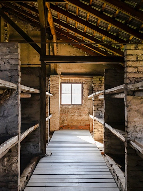 Auschwitz-Birkenau I barracks interior with wooden bunks and brick walls.