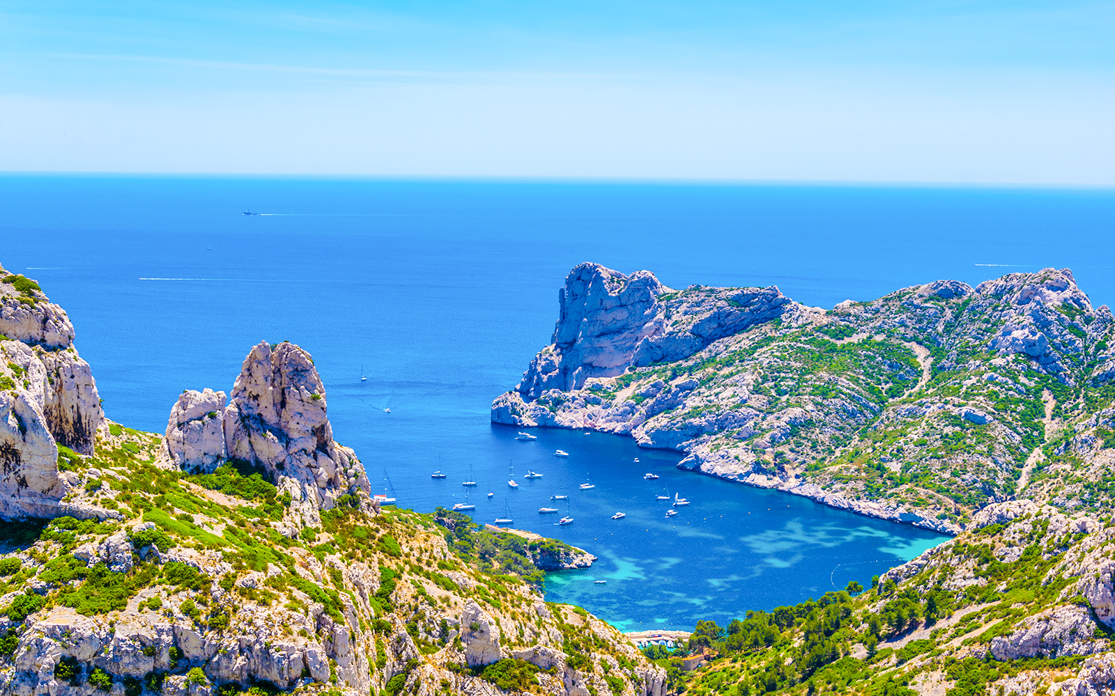 Boats anchored in the turquoise waters of Calanque de Sormiou, surrounded by rocky cliffs and greenery.
