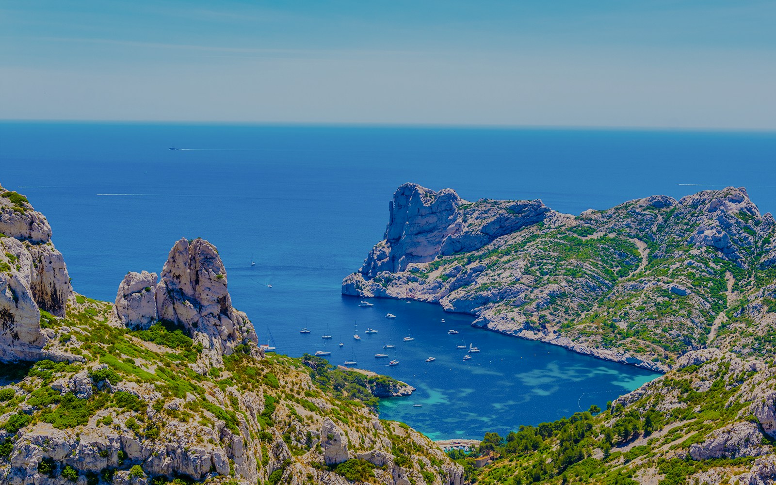 Boats anchored in the turquoise waters of Calanque de Sormiou, surrounded by rocky cliffs and greenery.