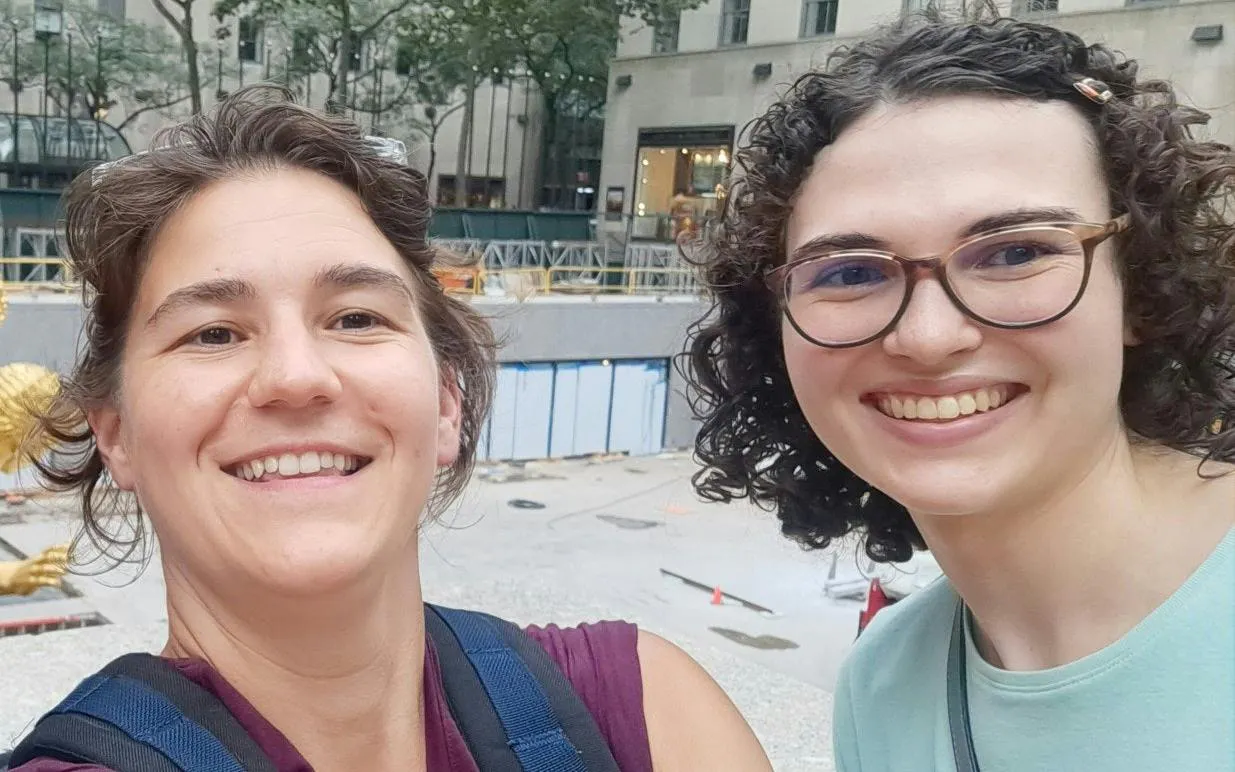 Two people smiling in front of Rockefeller Center, New York, during a self-guided city exploration game.