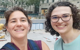 Two people smiling in front of Rockefeller Center, New York, during a self-guided city exploration game.