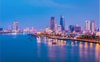 Da Nang skyline at night with illuminated buildings and river reflections.