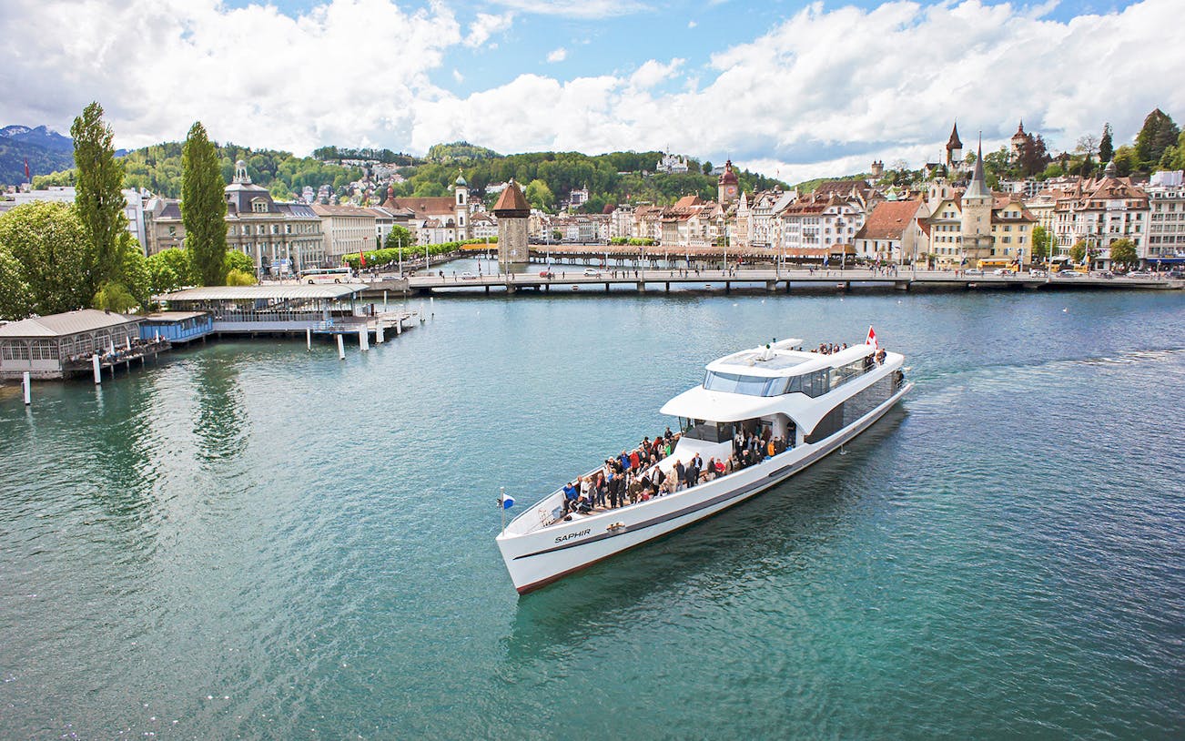 Panorama-yacht Saphir cruising on Lake Lucerne with cityscape in the background.