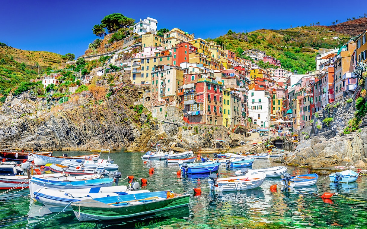 Boats in the harbor of Riomaggiore, Cinque Terre, with colorful hillside buildings.