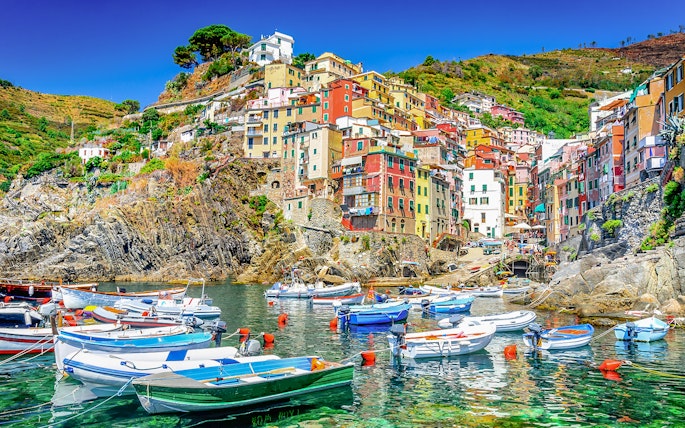 Boats in the harbor of Riomaggiore, Cinque Terre, with colorful hillside buildings.