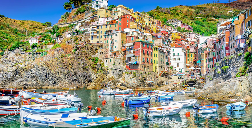 Boats in the harbor of Riomaggiore, Cinque Terre, with colorful hillside buildings.