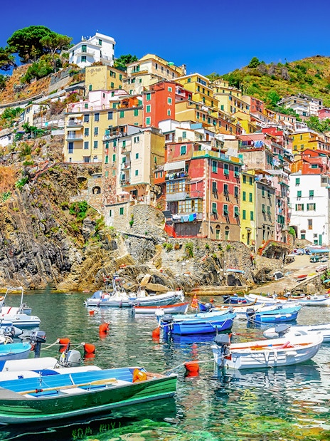 Boats in the harbor of Riomaggiore, Cinque Terre, with colorful hillside buildings.