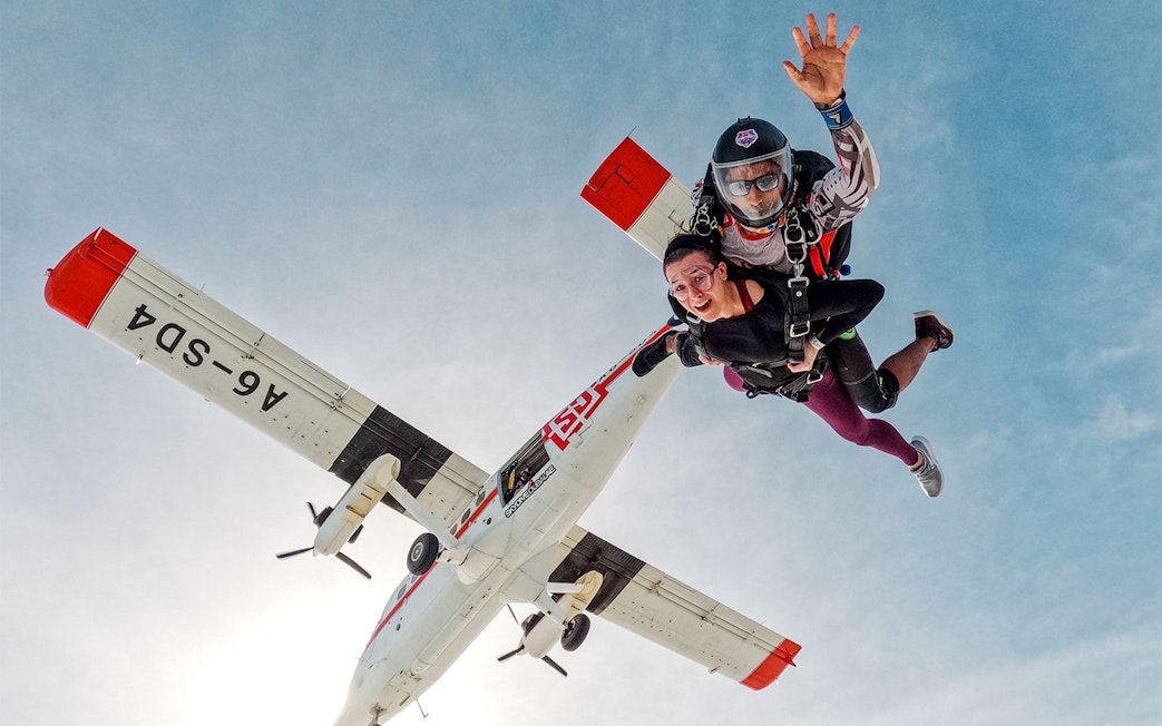 Skydivers tandem jumping from plane against clear sky.