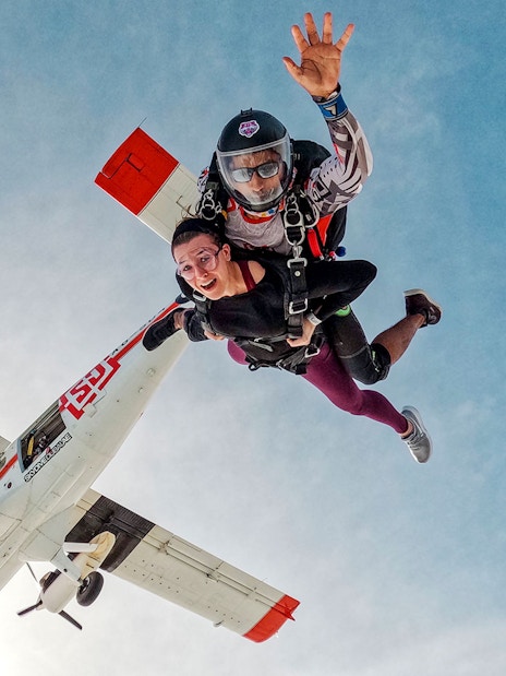 Skydivers tandem jumping from plane against clear sky.