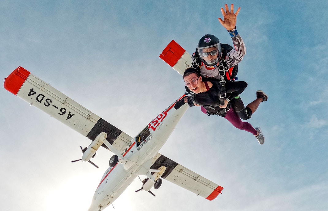 Skydivers tandem jumping from plane against clear sky.