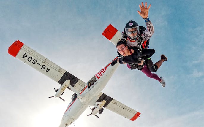 Skydivers tandem jumping from plane against clear sky.