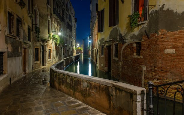 Venice canal at night with illuminated buildings and reflections on the water.