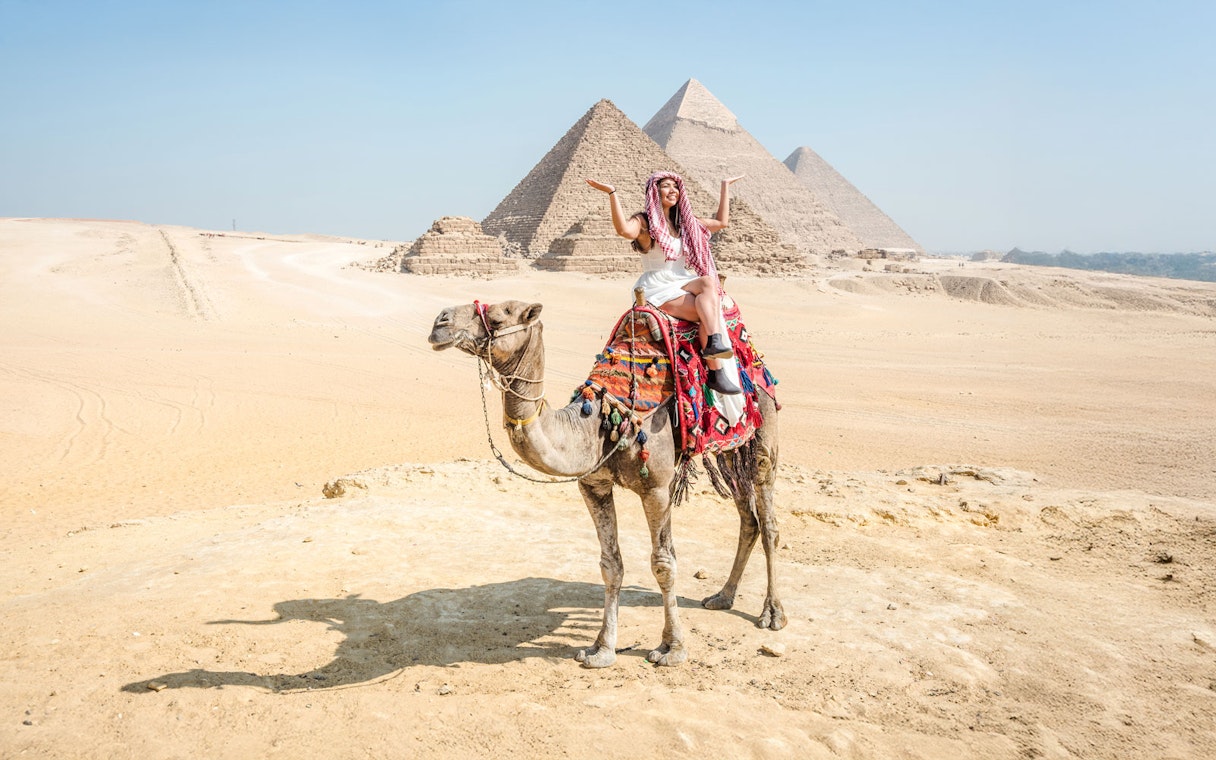 Tourist on camel with Giza Pyramids in background, Cairo guided tour.