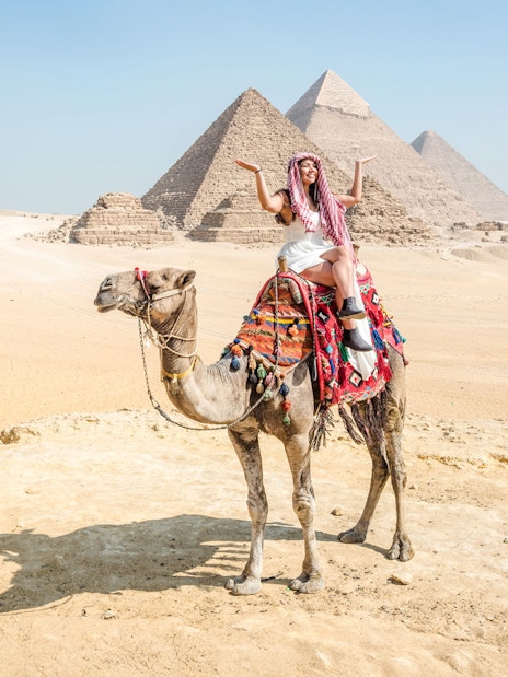 Tourist on camel with Giza Pyramids in background, Cairo guided tour.