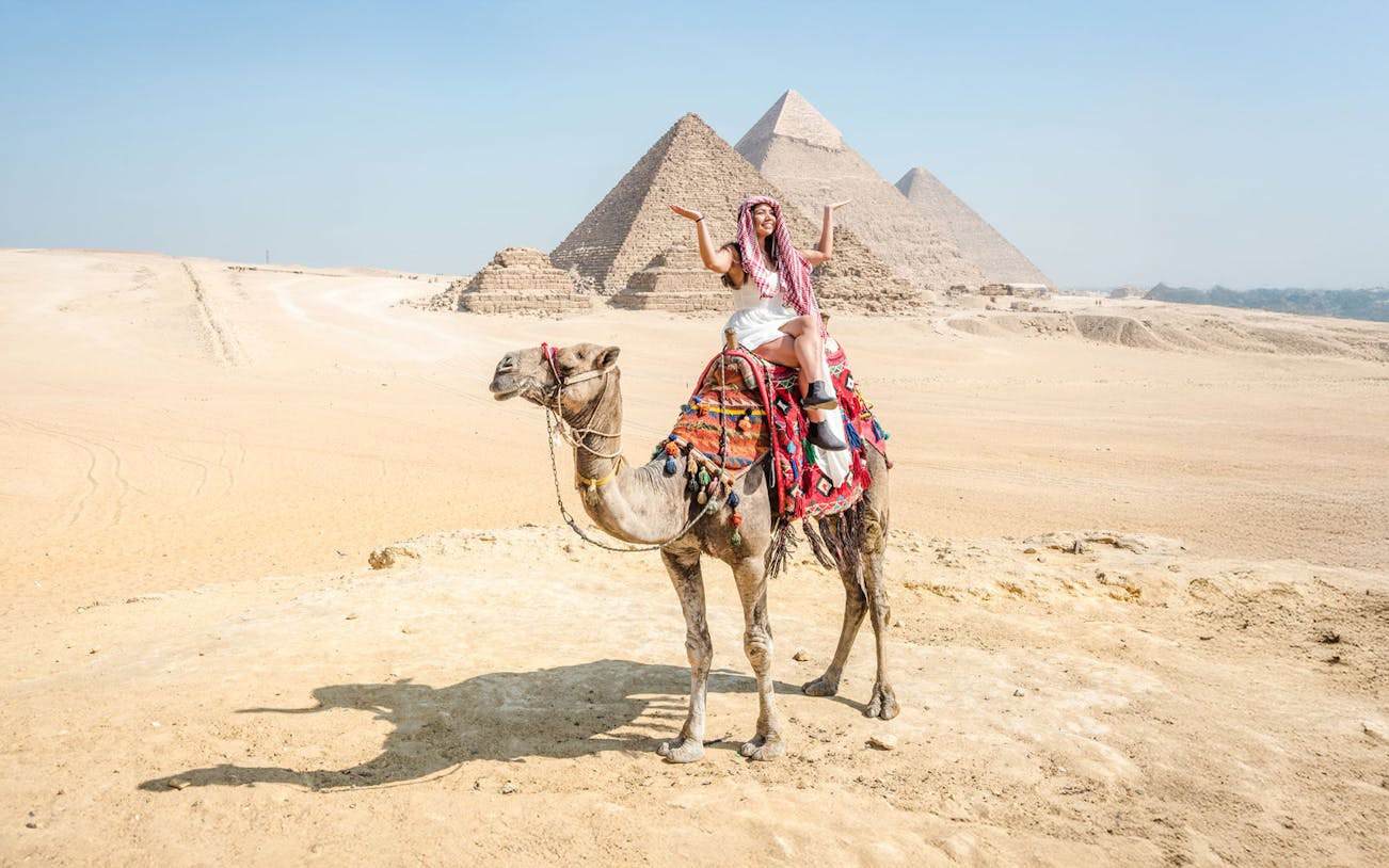 Tourist on camel with Giza Pyramids in background, Cairo guided tour.