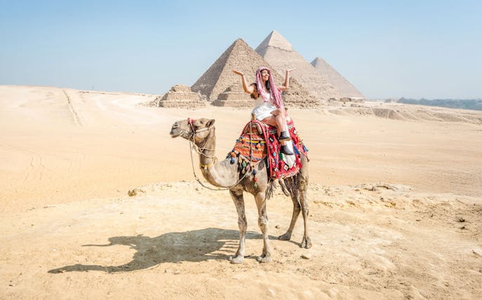 Tourist on camel with Giza Pyramids in background, Cairo guided tour.