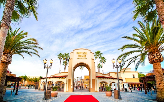 Entrance archway of Universal Studios Hollywood with palm trees and red carpet.