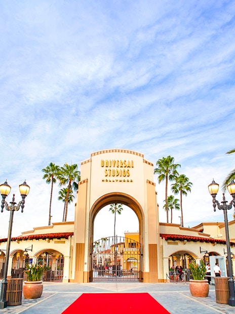 Entrance archway of Universal Studios Hollywood with palm trees and red carpet.
