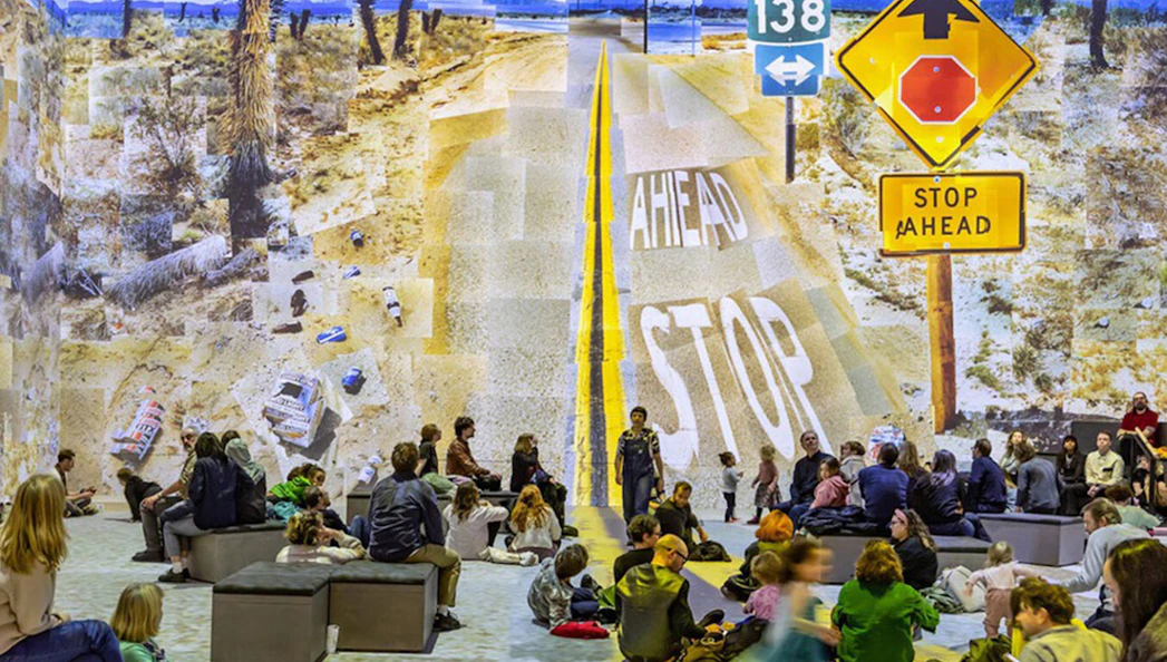 Visitors viewing David Hockney's "Bigger & Closer" exhibit with desert road collage.