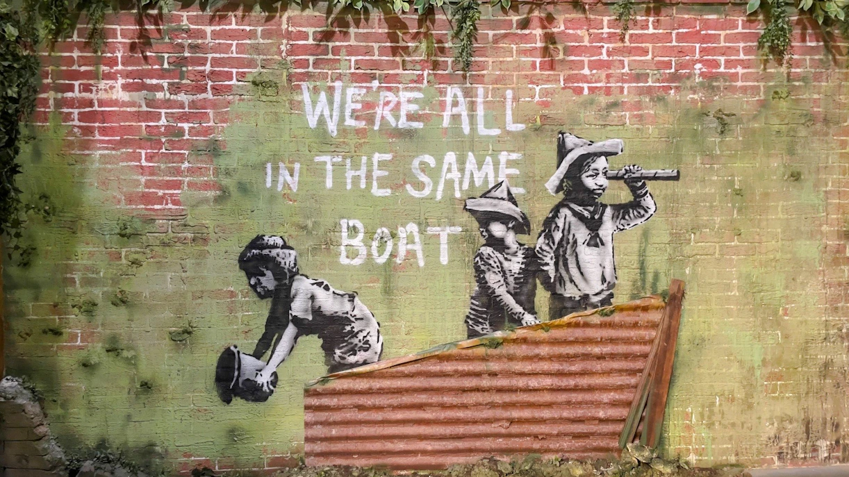 Street art of children with "We're all in the same boat" at Banksy Museum, Amsterdam.
