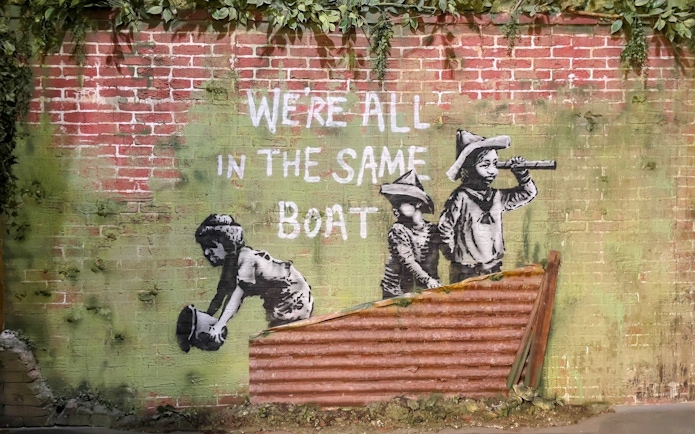 Street art of children with "We're all in the same boat" at Banksy Museum, Amsterdam.