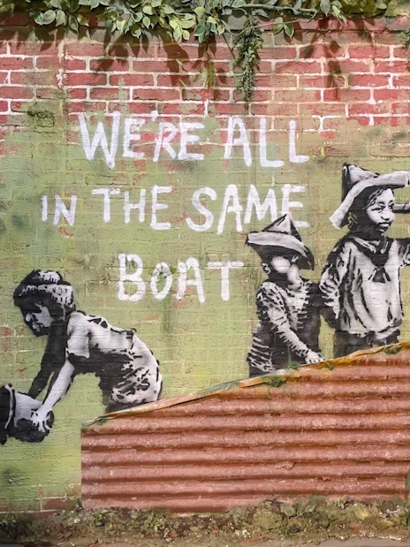 Street art of children with "We're all in the same boat" at Banksy Museum, Amsterdam.