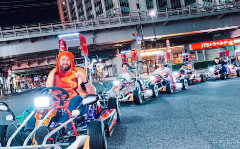 Go-kart riders in costume driving through Shibuya at night during NEO SHIBUYA EDGE experience.