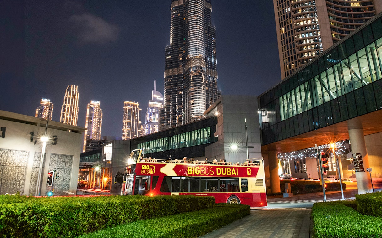Big Bus Dubai night tour passing by illuminated skyscrapers.