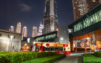 Big Bus Dubai night tour passing by illuminated skyscrapers.