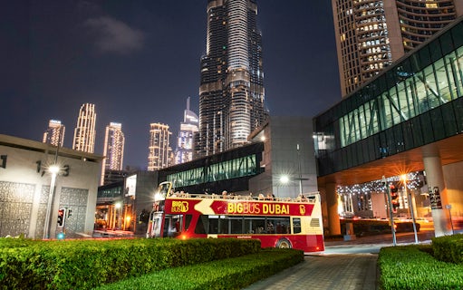 Big Bus Dubai night tour passing by illuminated skyscrapers.