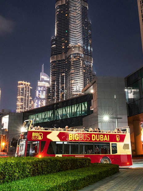 Big Bus Dubai night tour passing by illuminated skyscrapers.