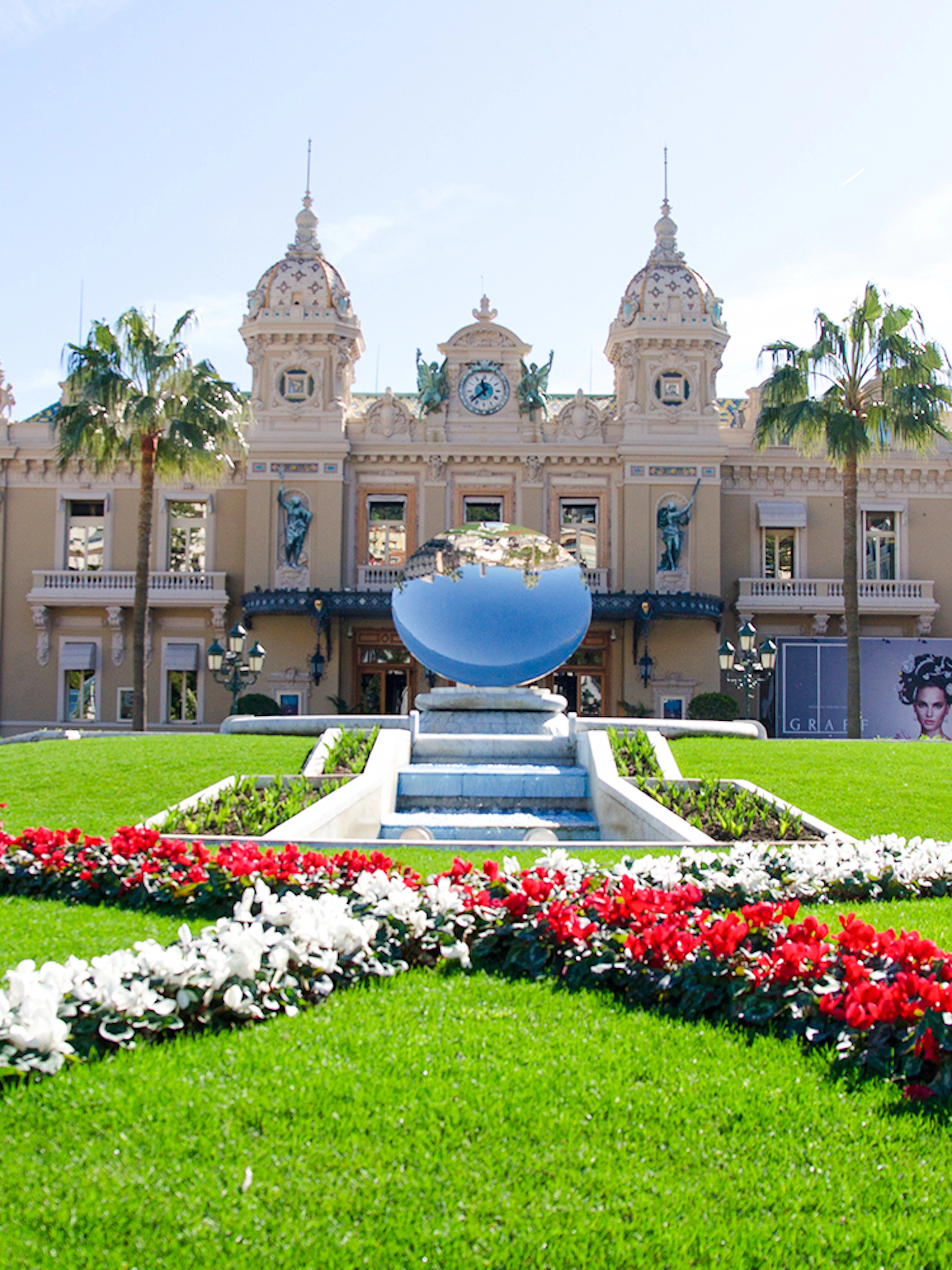 Monte Carlo Casino with gardens and reflective sculpture in front.
