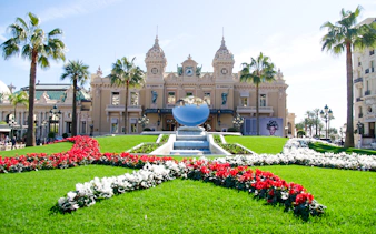Monte Carlo Casino with gardens and reflective sculpture in front.