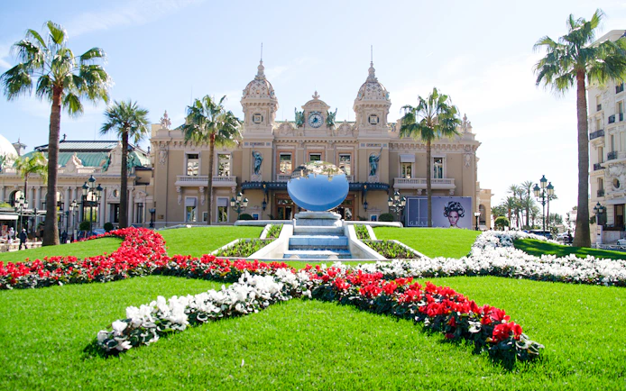 Monte Carlo Casino with gardens and reflective sculpture in front.