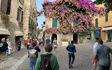 Tourists walking in a cobblestone street in Sirmione, Italy, with a stone building covered in vibrant flowers.