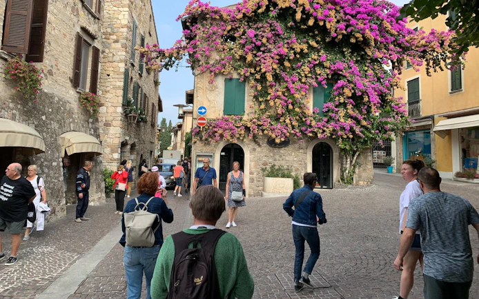 Tourists walking in a cobblestone street in Sirmione, Italy, with a stone building covered in vibrant flowers.