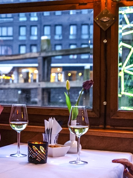 Guests enjoying wine on an Amsterdam Light Festival cruise with illuminated art outside.