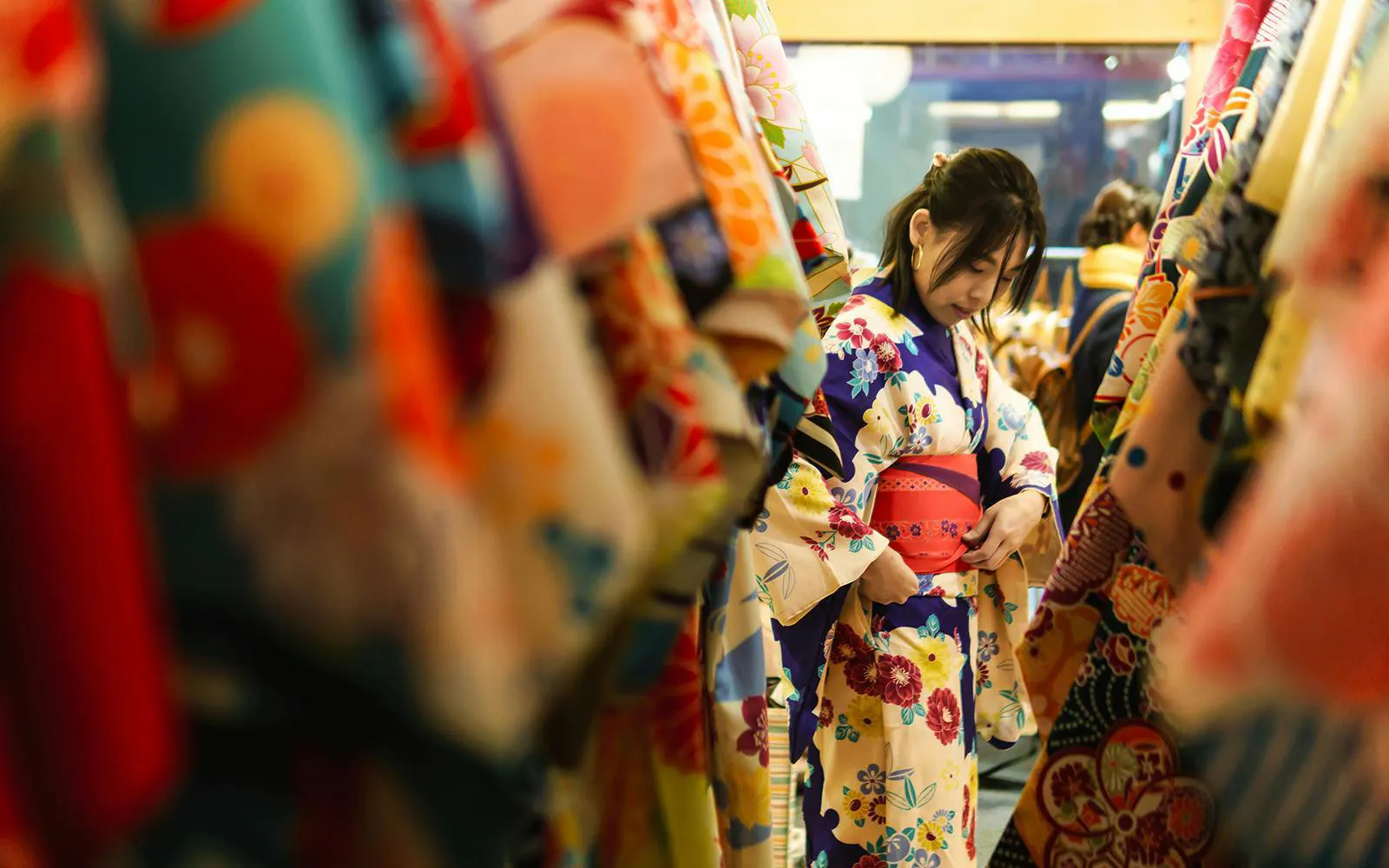 Young woman in kimono rental shop in Japan adjusting floral kimono.